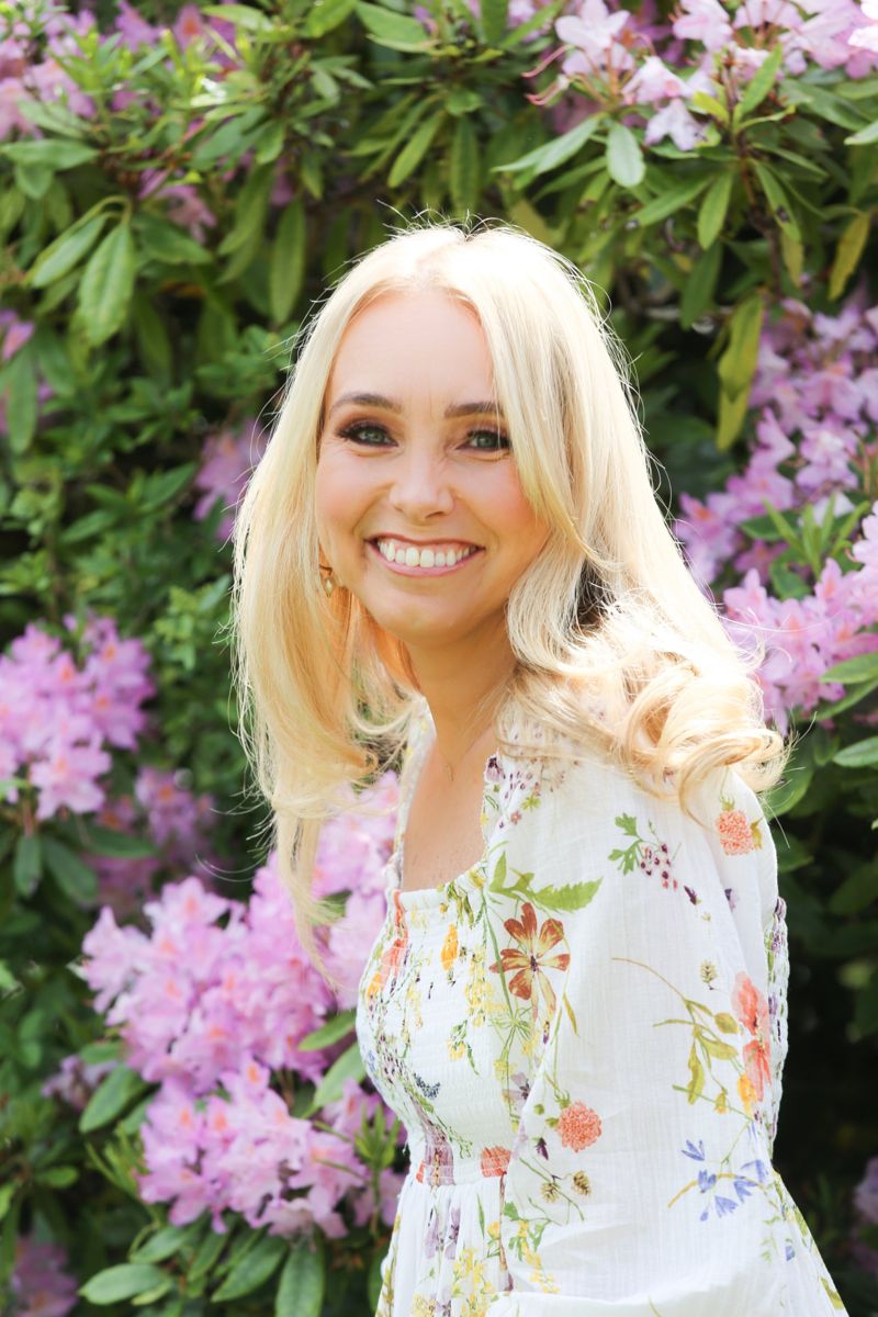 Business owner in a floral dress in front of rhododendrons